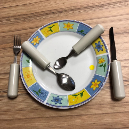 Couverts à manche grossis autour d'une assiette et posés sur une table en bois