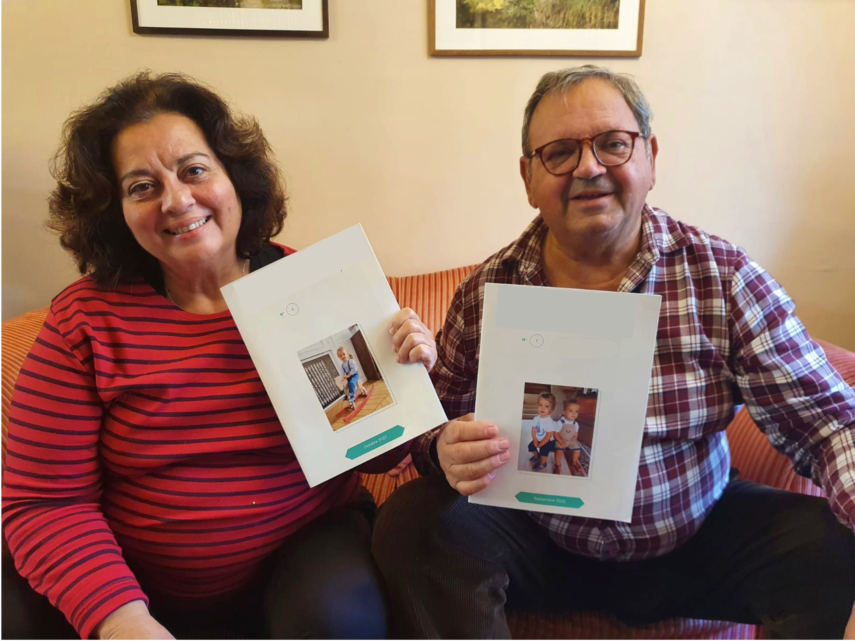 Photo d'une femme et d'un homme retraités, sourire aux lèvres, assis sur leur canapé chacun tenant un exemplaire d'un journal familial avec photos, montrant la page de couverture